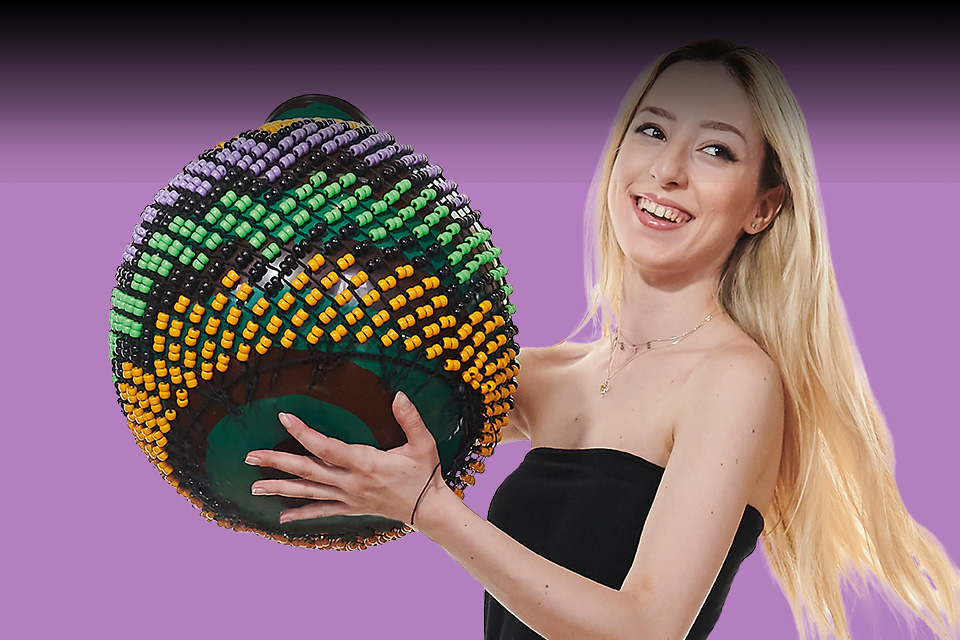 A blonde female student holding a percussion instrument, with a purple background
